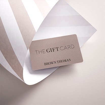 A Brown Thomas Gift Card rests on elegant wrapping paper, featuring muted striped patterns on a soft background.